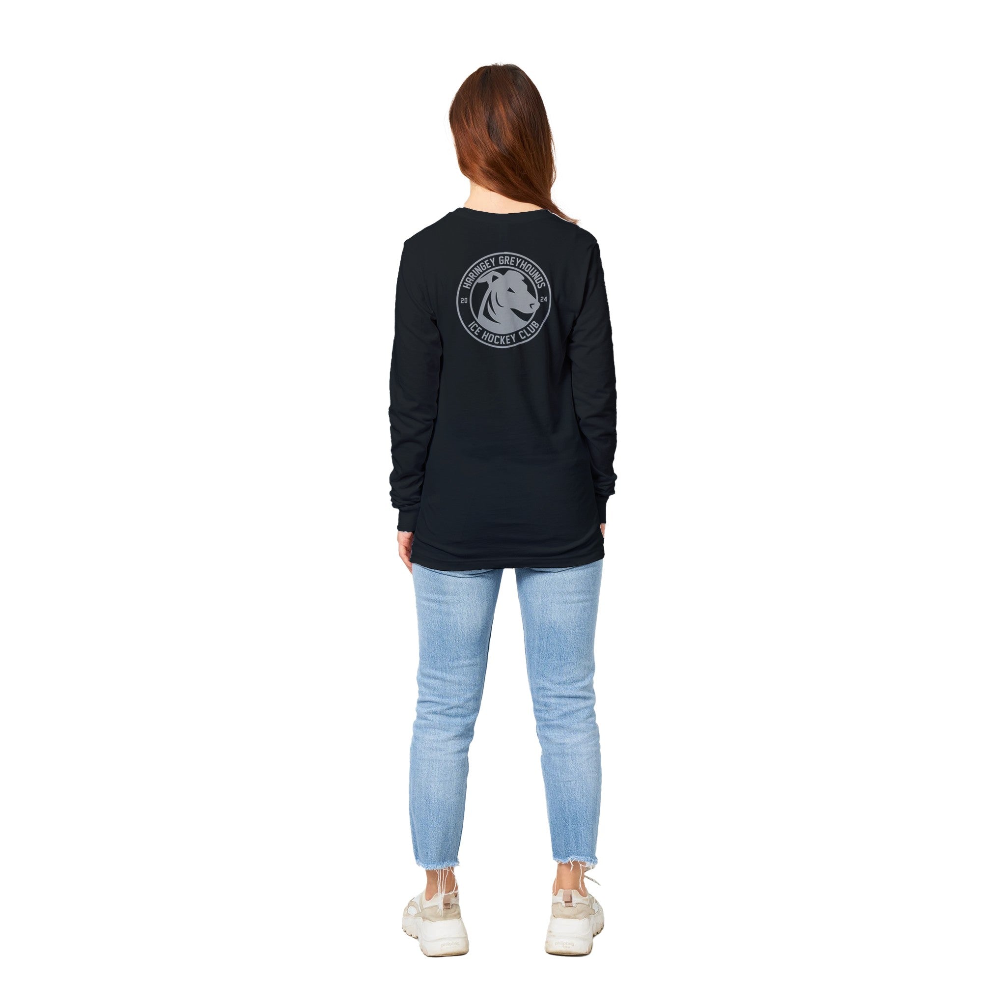 A person with long hair wears the Haringey Greyhounds Unisex Black Long Sleeve T-Shirt by Haringey Huskies Store, featuring a circular horse logo on the back, paired with light blue jeans and white sneakers. Check our size guide for your perfect fit.