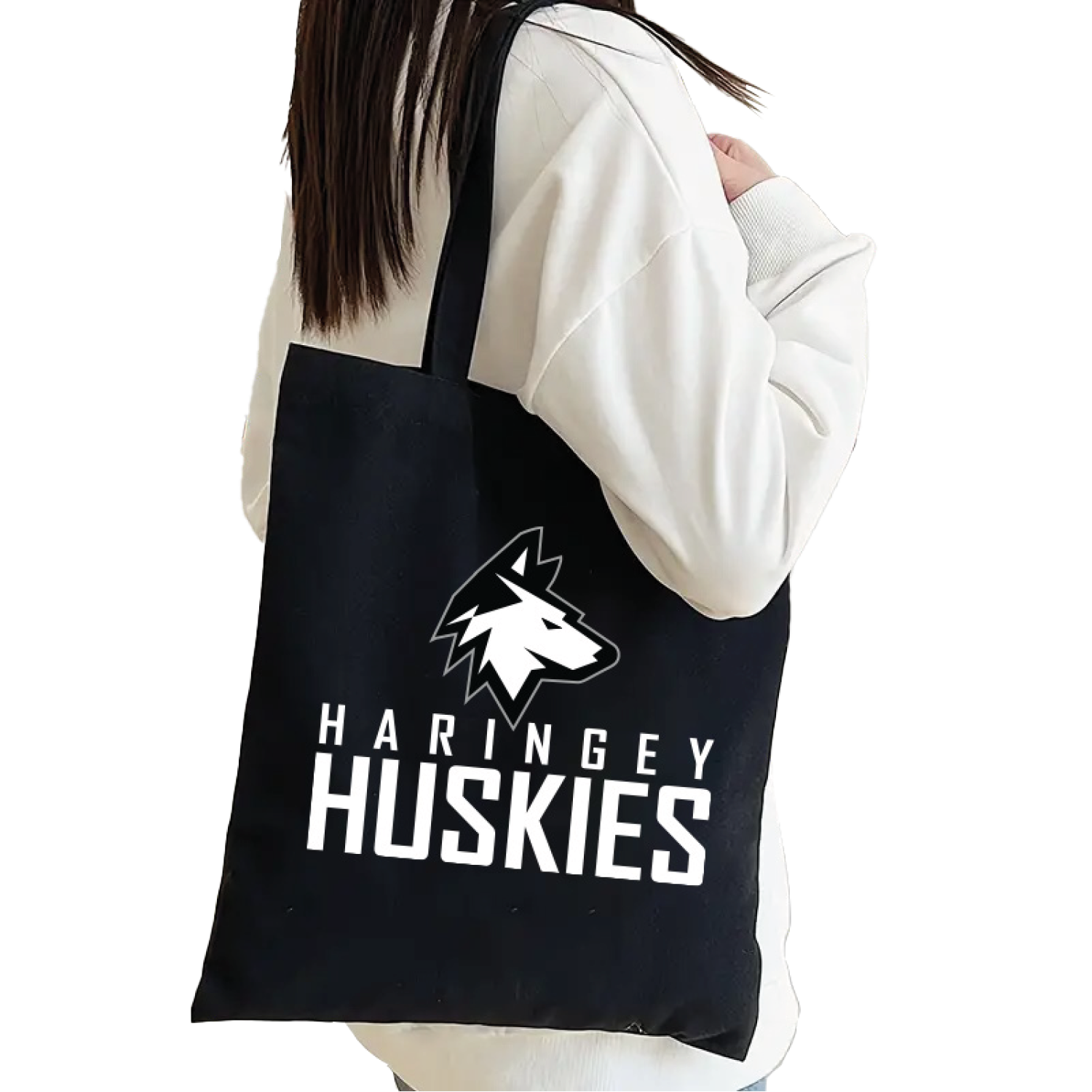 A person in a white jacket carries the Huskies Tote Bag Black Logo from the Haringey Huskies Store, featuring a bold wolf head and white HARINGEY HUSKIES text on durable fabric to show team pride.