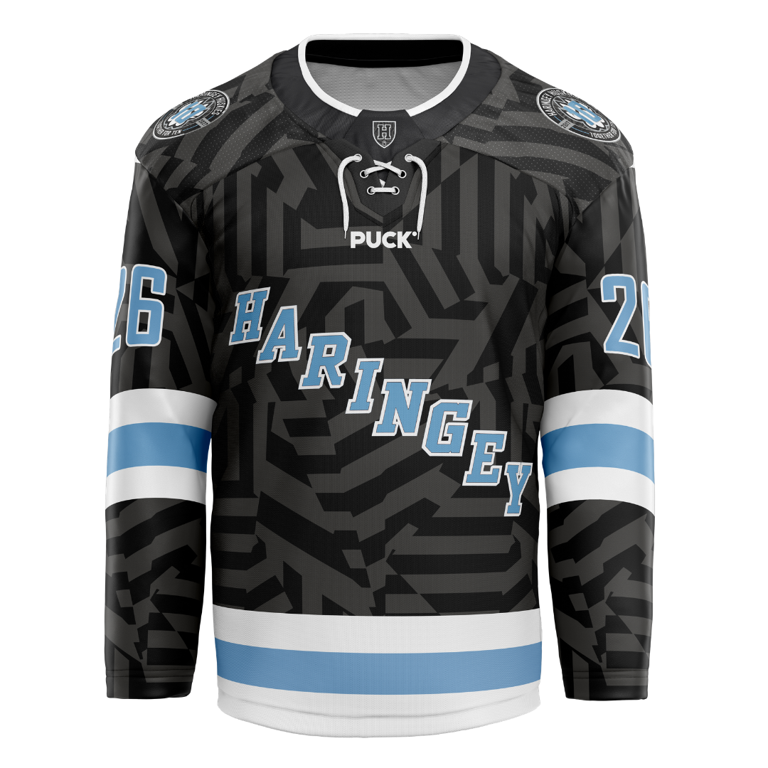 Introducing the Haringey Huskies 26/27 Away Jersey (NAMED) from the Haringey Huskies Store—a black hockey jersey featuring bold geometric patterns, light blue and white stripes on the arms and waist, "HARINGEY" in light blue letters across the chest, and the number 26 on both sleeves. Available as a Fan Replica Jersey, you can personalize it with your own custom name and number for a unique touch.