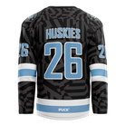 Back view of the Haringey Huskies 26/27 Away Jersey (NAMED) from the Haringey Huskies Store, featuring light blue and white accents, HUSKIES and the number 26 in large light blue font, and a pattern of dark geometric shapes. The word PUCK appears near the bottom. This jersey can be customized with your own name and number.