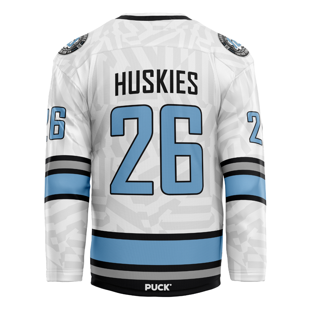 The Haringey Huskies 26/27 Home Jersey (NAMED) from the Haringey Huskies Store is a white fan replica jersey with black and blue stripes, featuring the number 26 and "Huskies" on the back, along with the word PUCK above the lower hem.