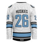 The Haringey Huskies 26/27 Home Jersey (NAMED) from the Haringey Huskies Store is a white fan replica jersey with black and blue stripes, featuring the number 26 and "Huskies" on the back, along with the word PUCK above the lower hem.
